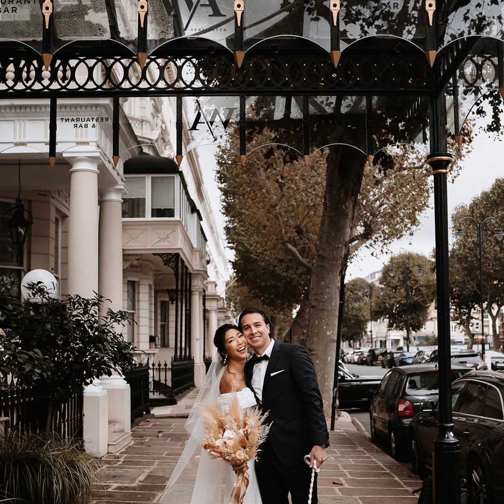 Joyful Bride and Groom smile in Chelsea with Cockapoo dressed in his doggy suit 