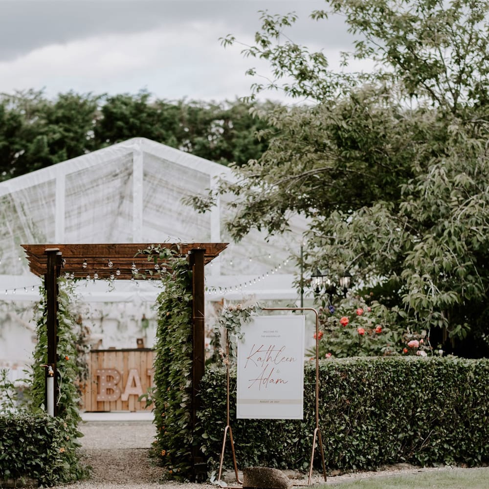 White clear sided marquee in garden with wooden bar and greenery for DIY garden wedding in Bedfordshire 
