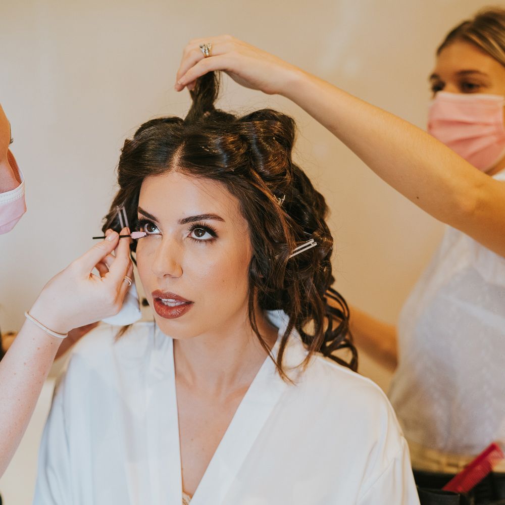 Bride in white robe with brown hair in rollers gets her makeup and hair done before Notley Abbey wedding