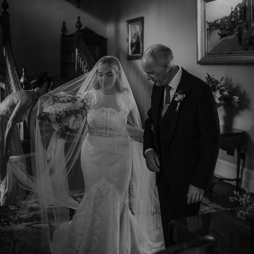 Bride in a Jesus Piero lace cap sleeve wedding dress with her father on the morning of the wedding 