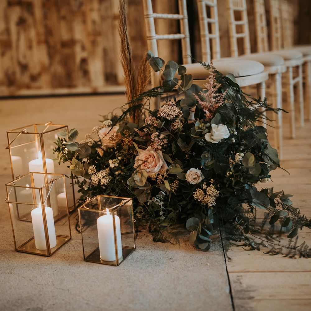 Pink, white and green floral aisle decor with white pillar candles in gold glass candle holders for rustic wedding