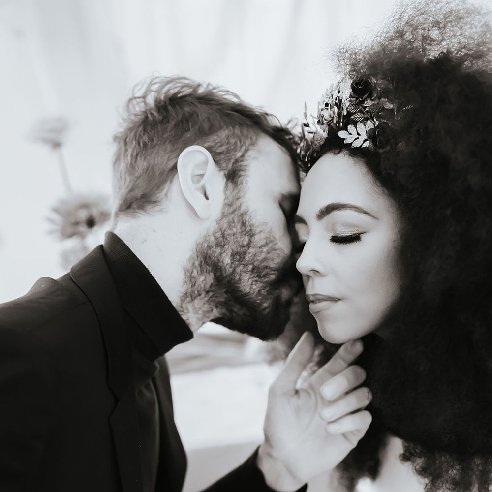 Black and white picture of the groom nuzzling his Black bride with naturally curly afro hair's neck. 