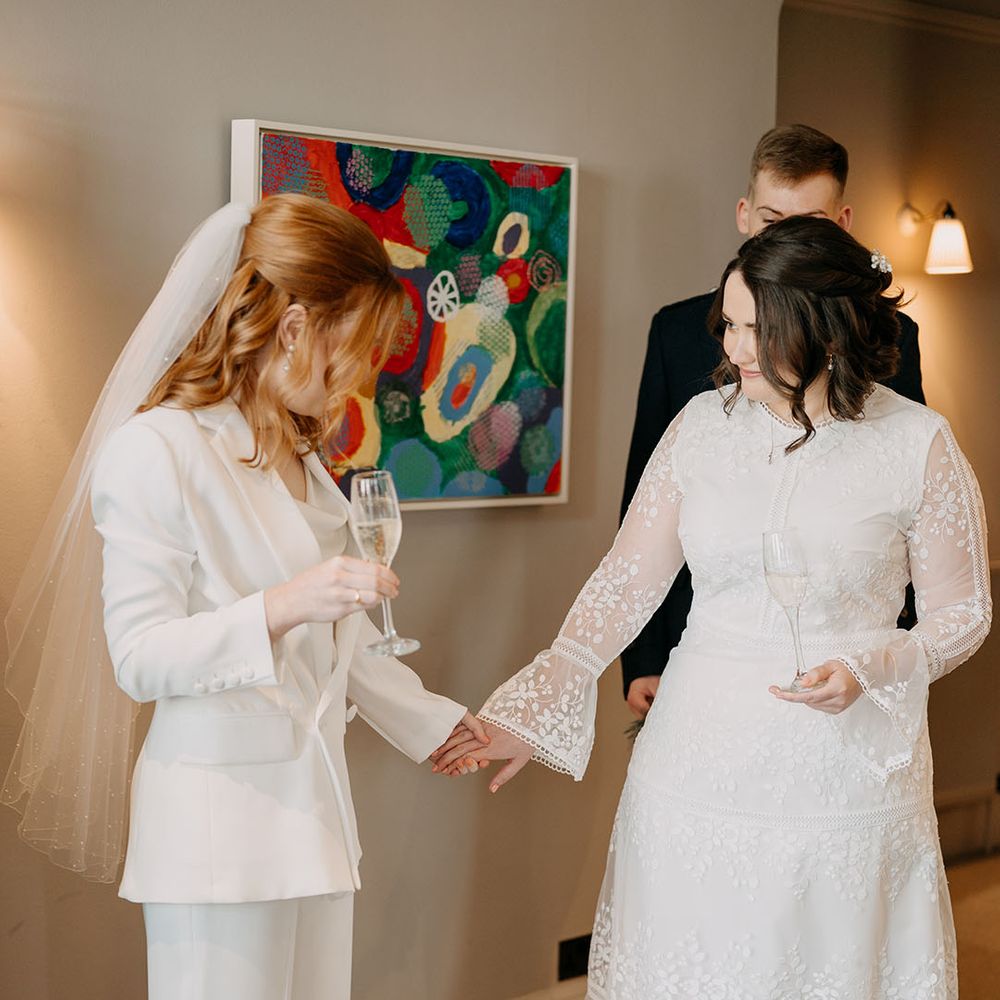 Brides hold flutes of champagne and look at one another on their wedding day