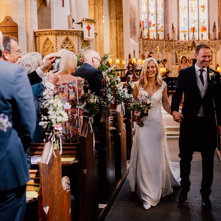 Bride in lace wedding dress walks back down the aisle with groom in morning suit with grey waistcoat as they are a married couple 