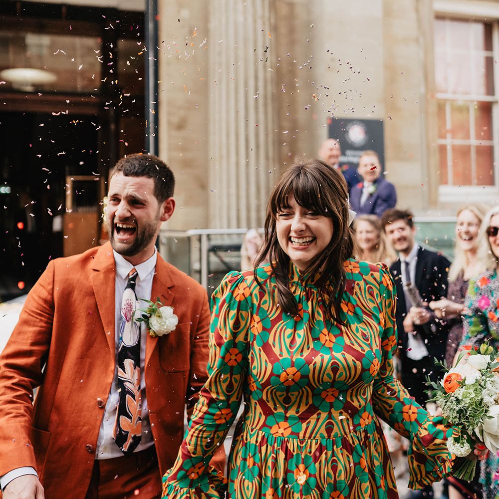 Bride & groom smile brightly as they walk through confetti outdoors on their wedding day