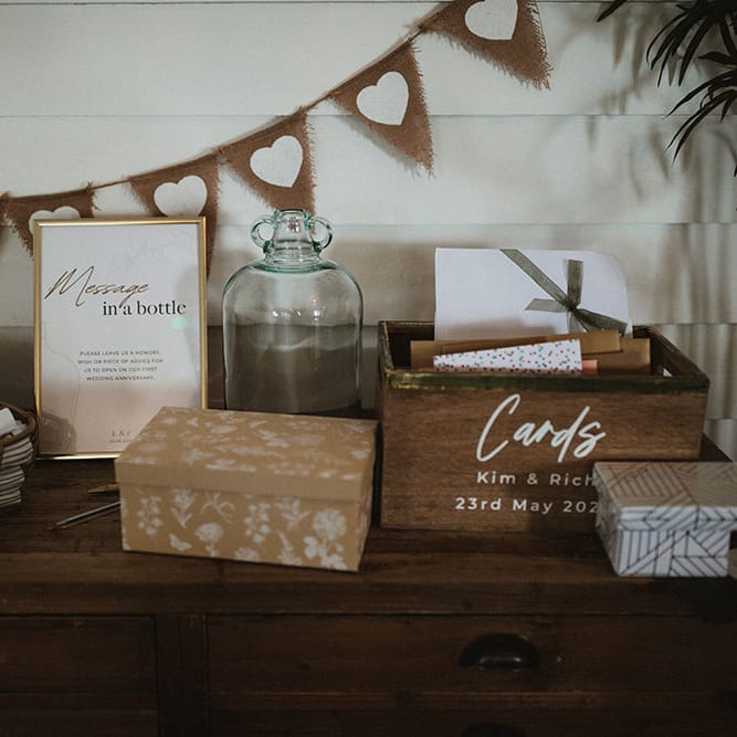 Wooden table with heart bunting behind for cards and 'Message In A Bottle' alternative guest book idea