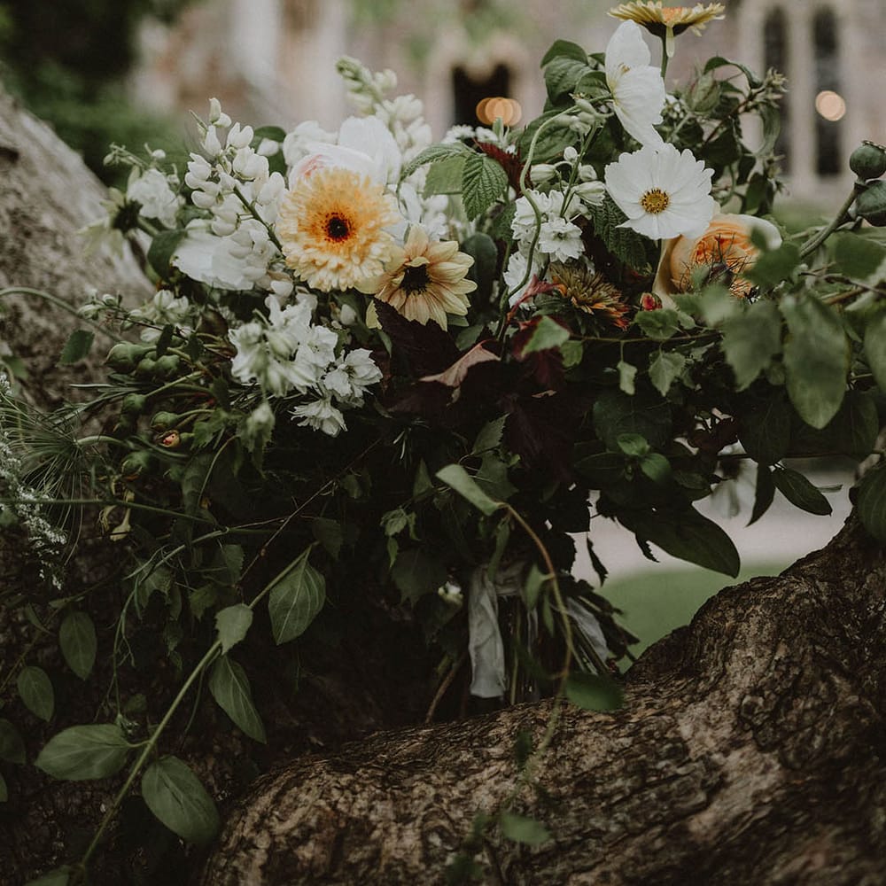 oversized green foliage, white and yellow flower wedding bouquet resting on a tree