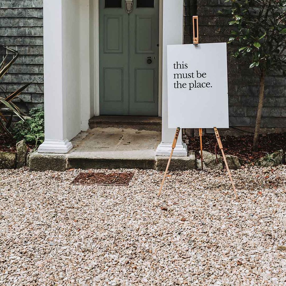Grey door at Treseren wedding venue with white "this must be the place" minimal wedding sign on wooden easel