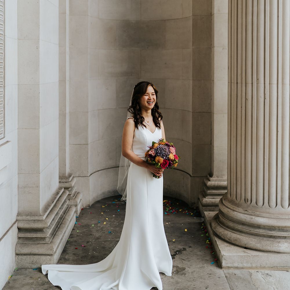 Bride holds colourful floral bouquet and wears elegant classic wedding dress 