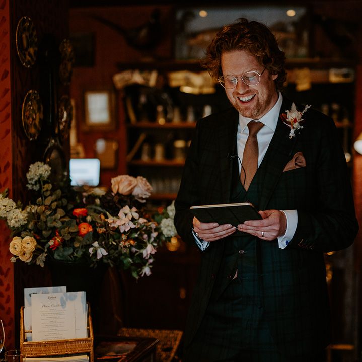 Groom in dark suit with orange tie, orange pocket square and autumnal boutonniere doing wedding reading 