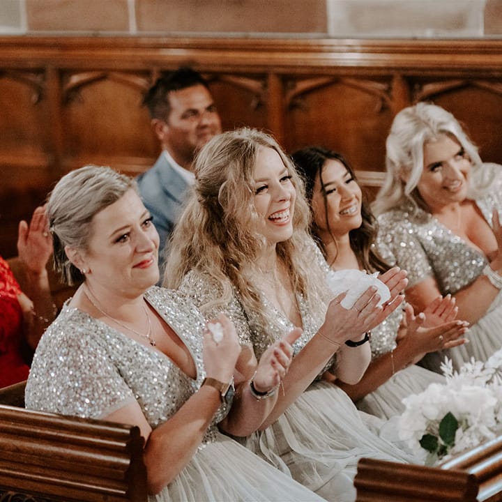 Bridesmaids sit in matching pre loved sequin silver dresses and clap for the bride and groom 