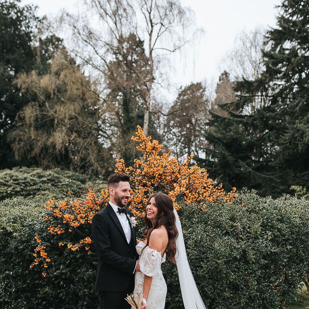 The groom smiles brightly as he embraces the bride in a boho bridal outfit on their wedding day at Hampton Manor 