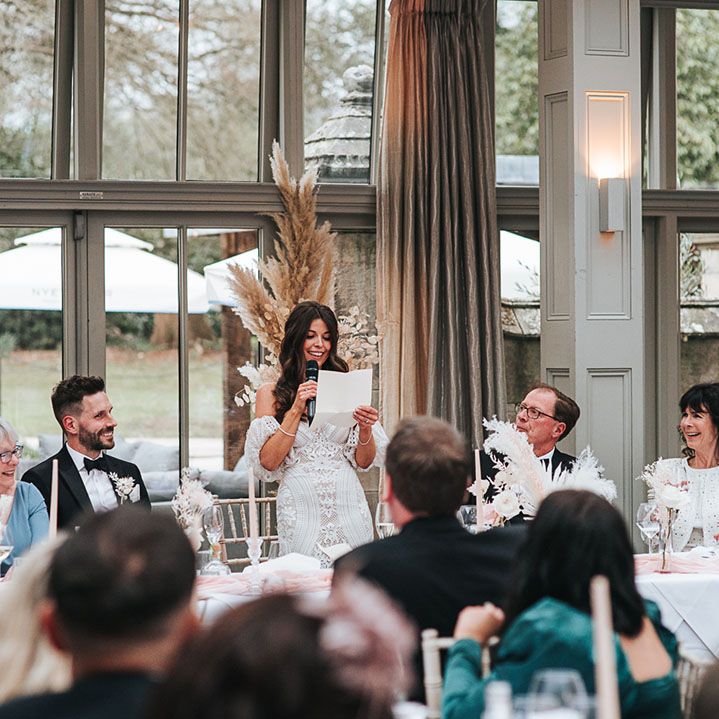 The bride stands up holding a microphone as she delivers her bridal speech 