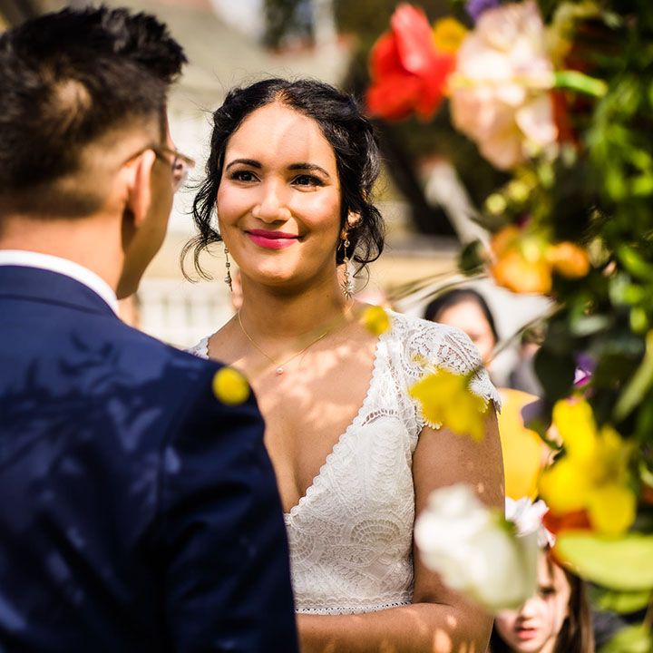 Bride in lace wedding dress looks lovingly toward her groom during outdoor wedding ceremony