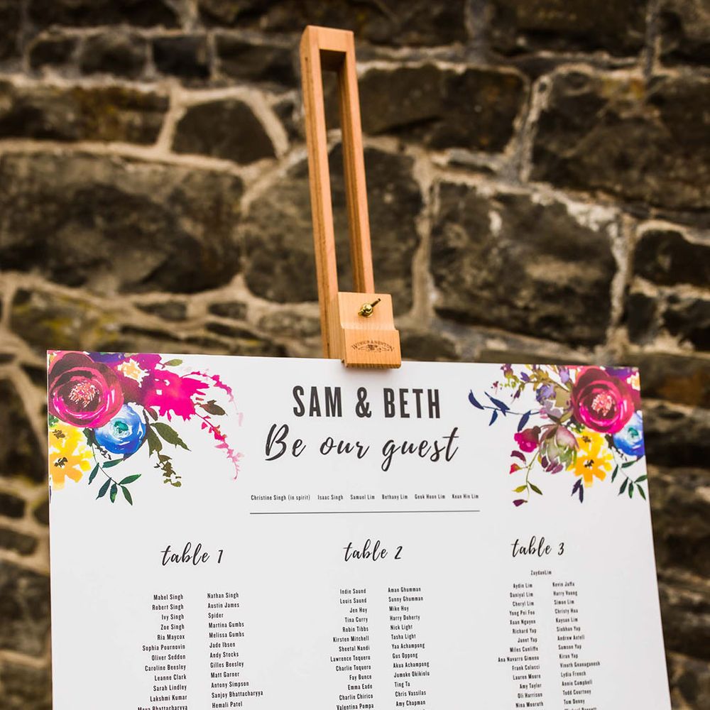 White seating chart complete with colourful floral illustrations on wooden easel 