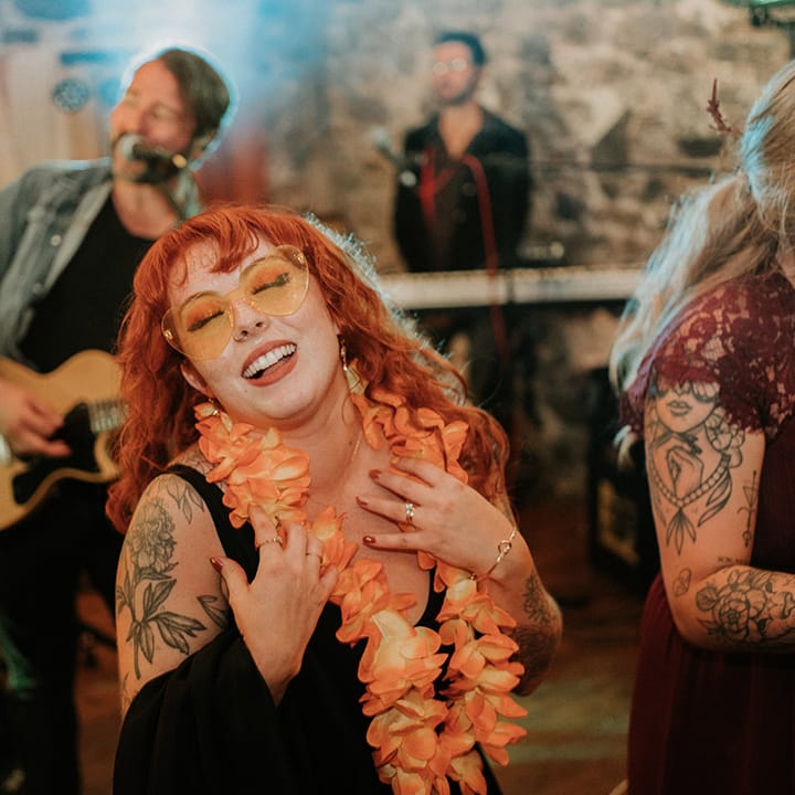 Bride in v neck black wedding dress, orange wedding lei and orange wedding sunglasses dancing 