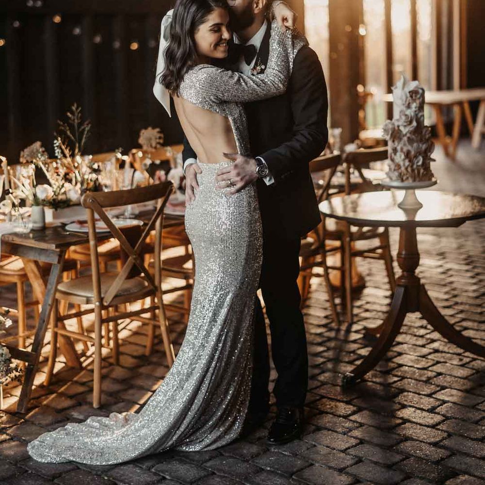 Groom in classic black tuxedo dancing with bride in open back silver sparkly wedding dress and large hair bow accessory 