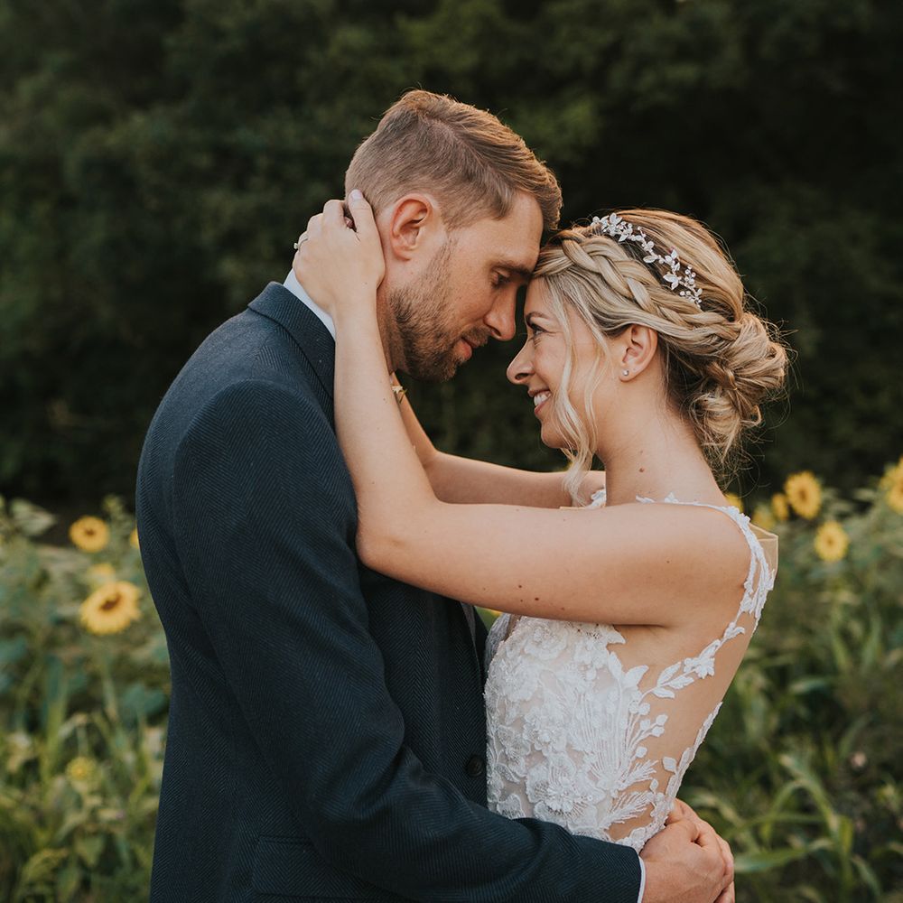 The bride with her blonde hair in a braided updo with sparkly headpiece in a illusion lace wedding dress and the groom in a dark blue suit 