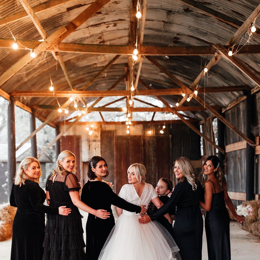 Bridesmaids in mismatched black bridesmaid dresses posing with the bride for bridal party shots at Silchester Farm