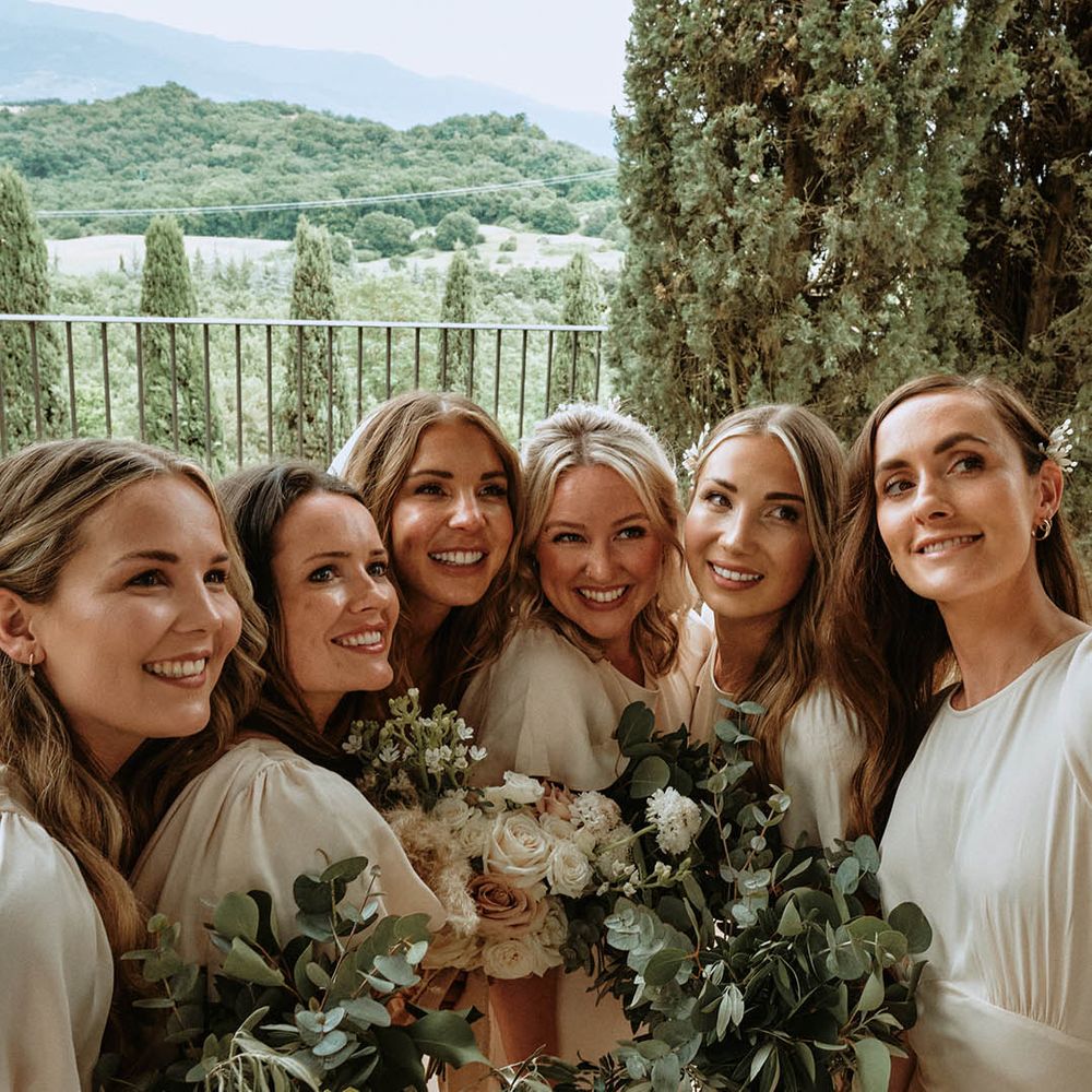 Bride and bridesmaids in off white satin bridesmaids dresses taking a selfie while holding eucalyptus bridesmaid bouquets