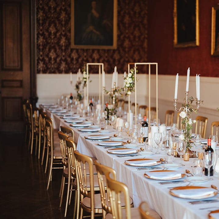 Classic wedding tablescape with white table cloth, tapered candles in gold candelabras, gold frame decorations, gold plates, gold cutlery and dried flower and white rose floral arrangements at Grittleton House 