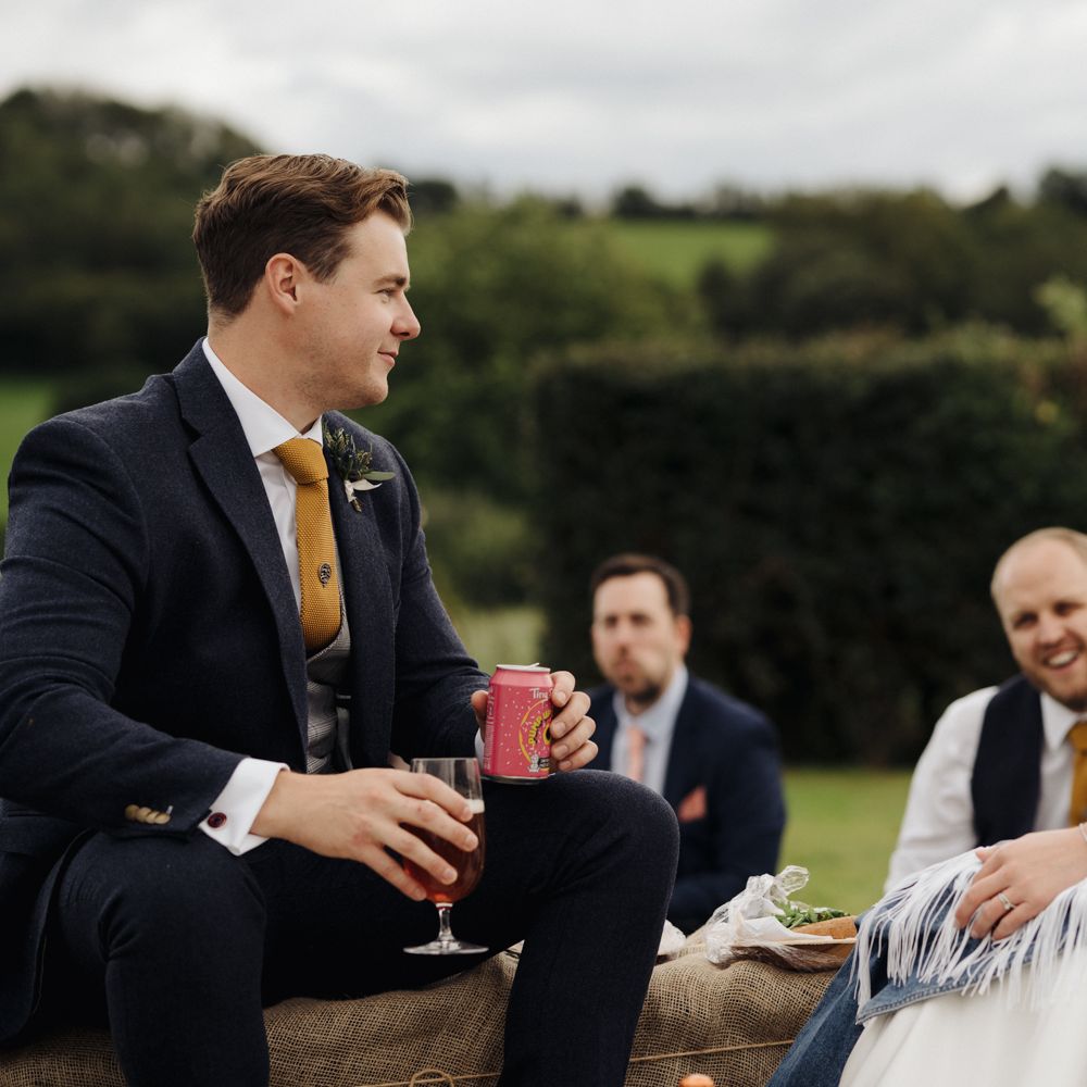 Bride & groom sat on hay bales in garden with wedding guests 