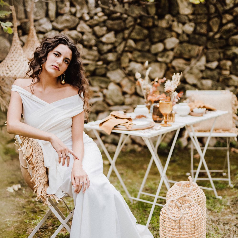 Bride sits outdoors in Mallorca next to woven candle holders