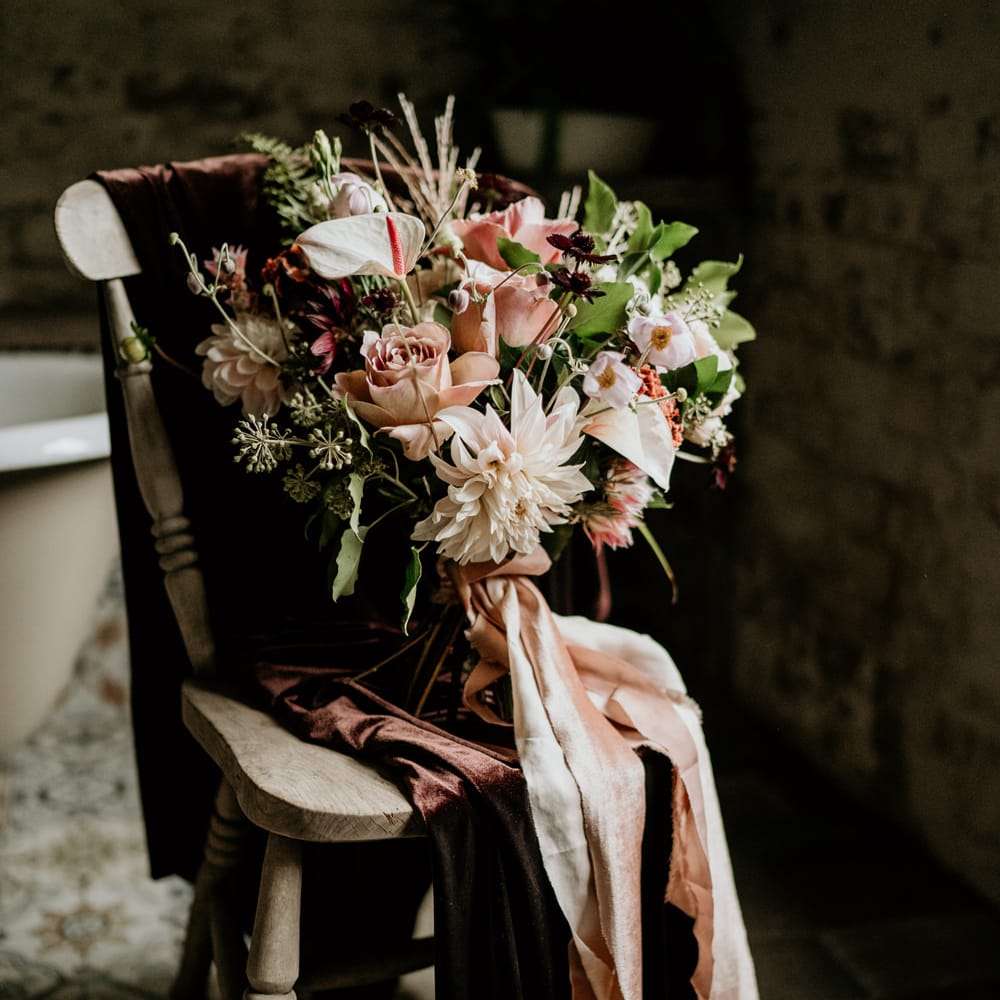 Pink wedding bouquet with dahlias, roses and anthuriums tied with ribbon sitting on a wooden chair 