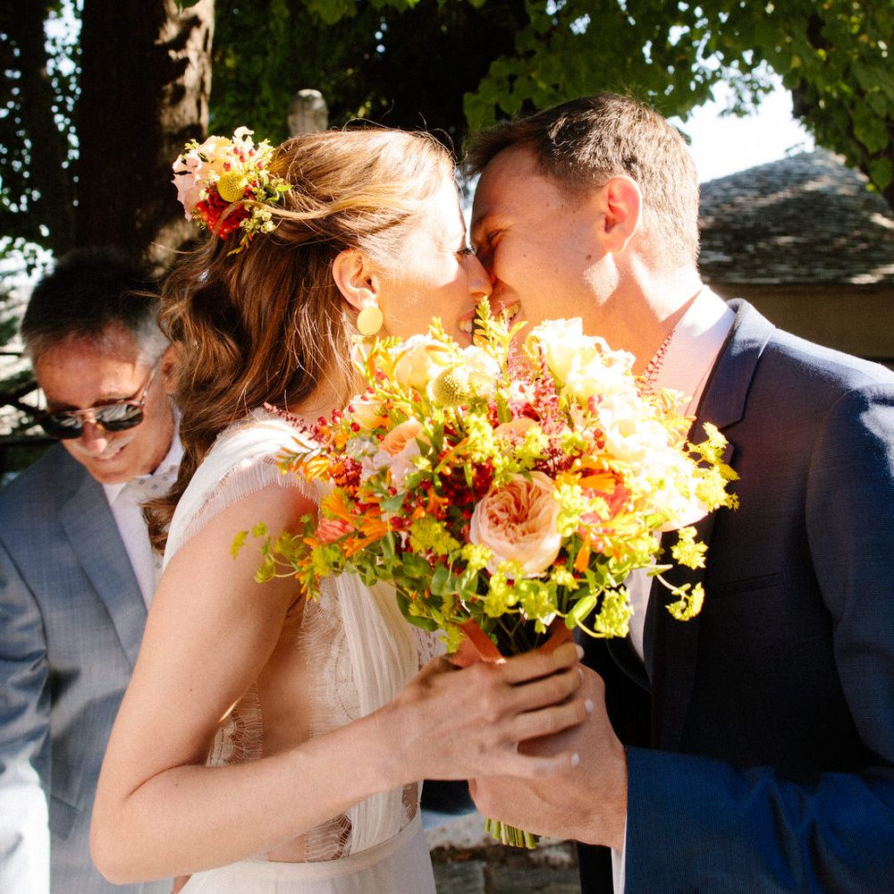 The bride and groom share a kiss behind her bouquet