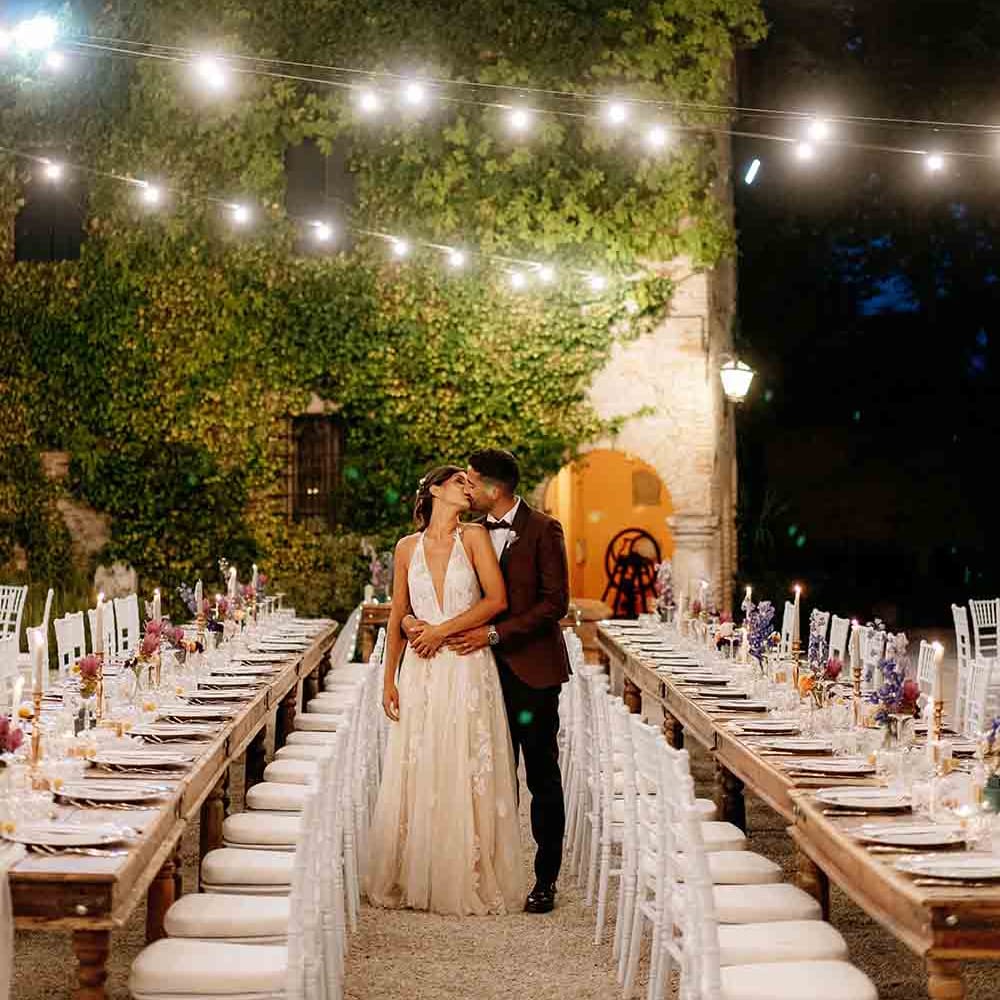 Festoon lighting hangs over long tables for wedding