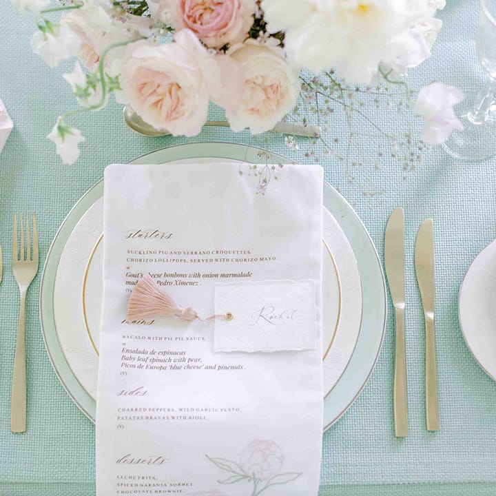 elegant place setting with gold rimmed plates, pale green tablecloth and fabric menu 