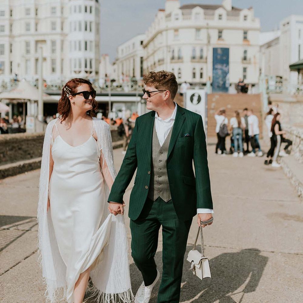 Bride & groom walk hand in hand on their wedding day through Brighton as they both wearing sunglasses on their wedding day