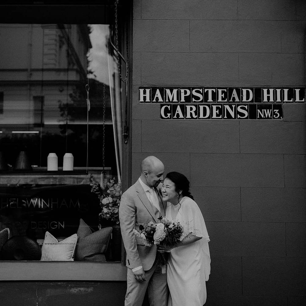 Bride & groom stand outdoors as they lovingly embrace on their wedding day in black & white image 