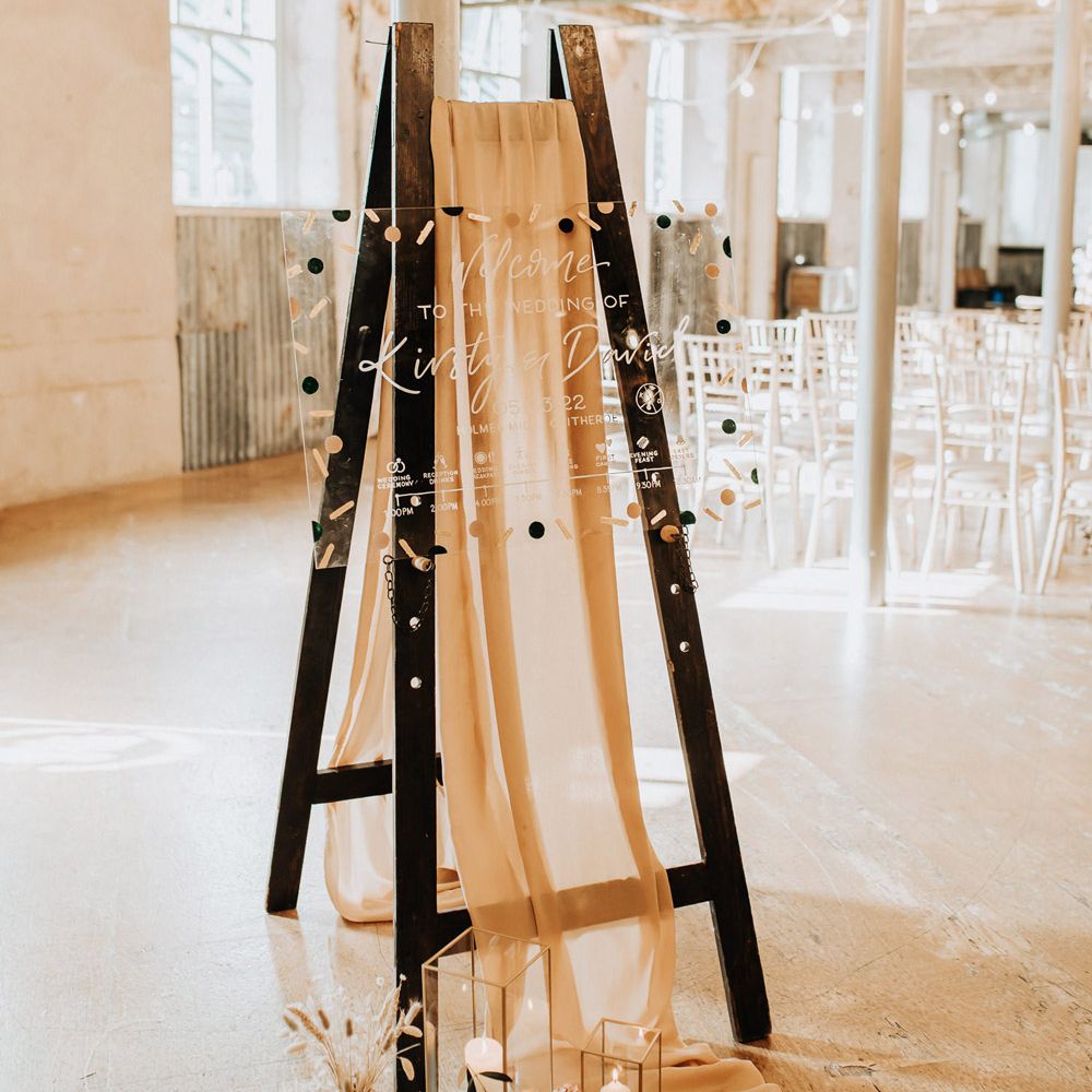 Acrylic wedding welcome sign with confetti design on black easel with draping at industrial wedding reception