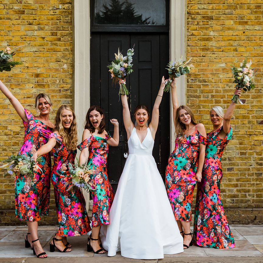Bride in v neck wedding dress celebrates with her bridesmaids in bright floral dresses at London wedding
