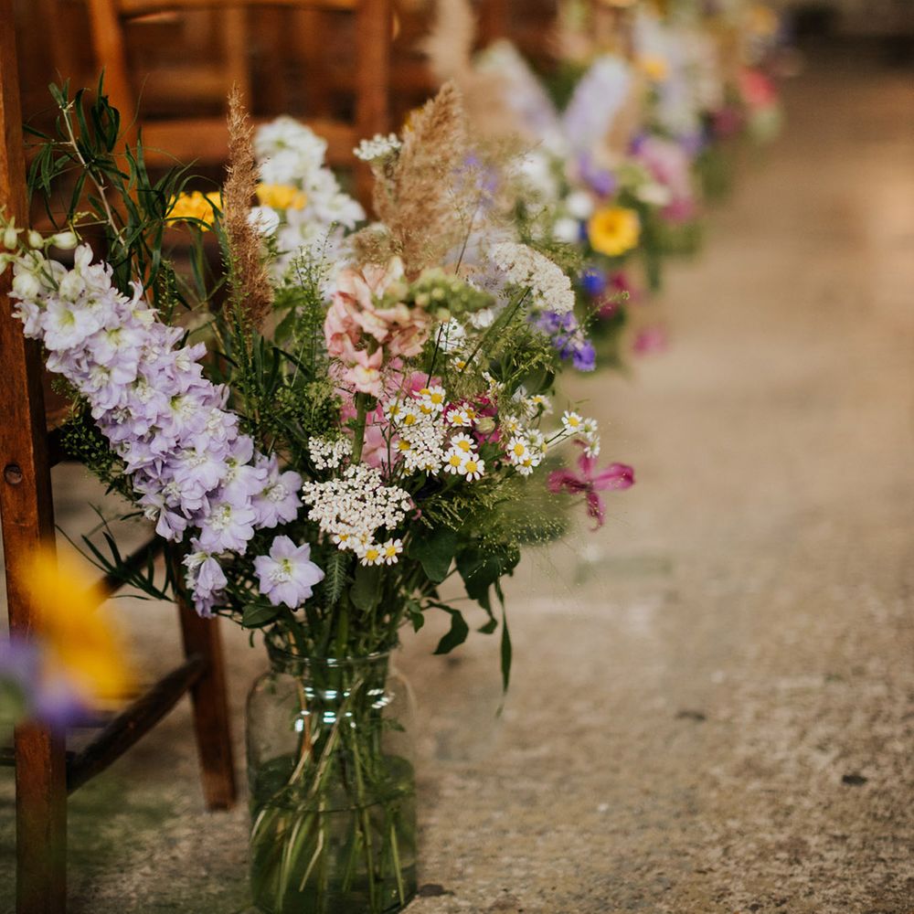Pretty and colourful flowers in glass vases as aisle wedding decor 