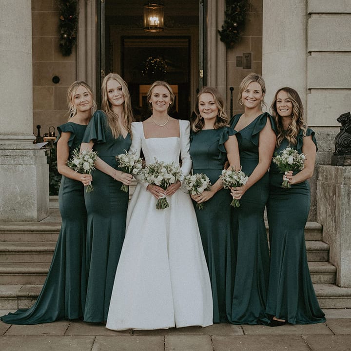 Bridal squad wearing Suzanne Neville, long white wedding dress and long bottle green dresses with white mixed floral bouquets