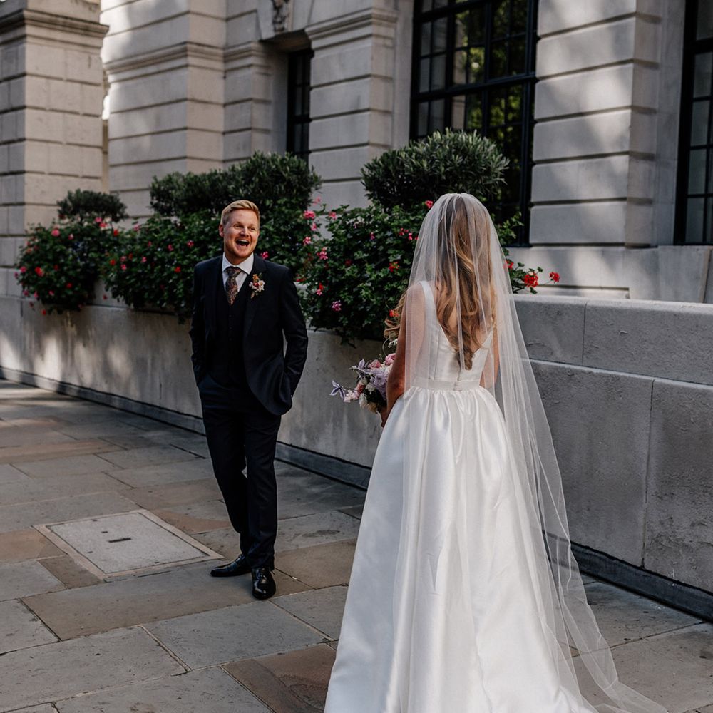 Bride in a princess wedding dress and long veil approaching her husband in a navy suit at their romantic first look 