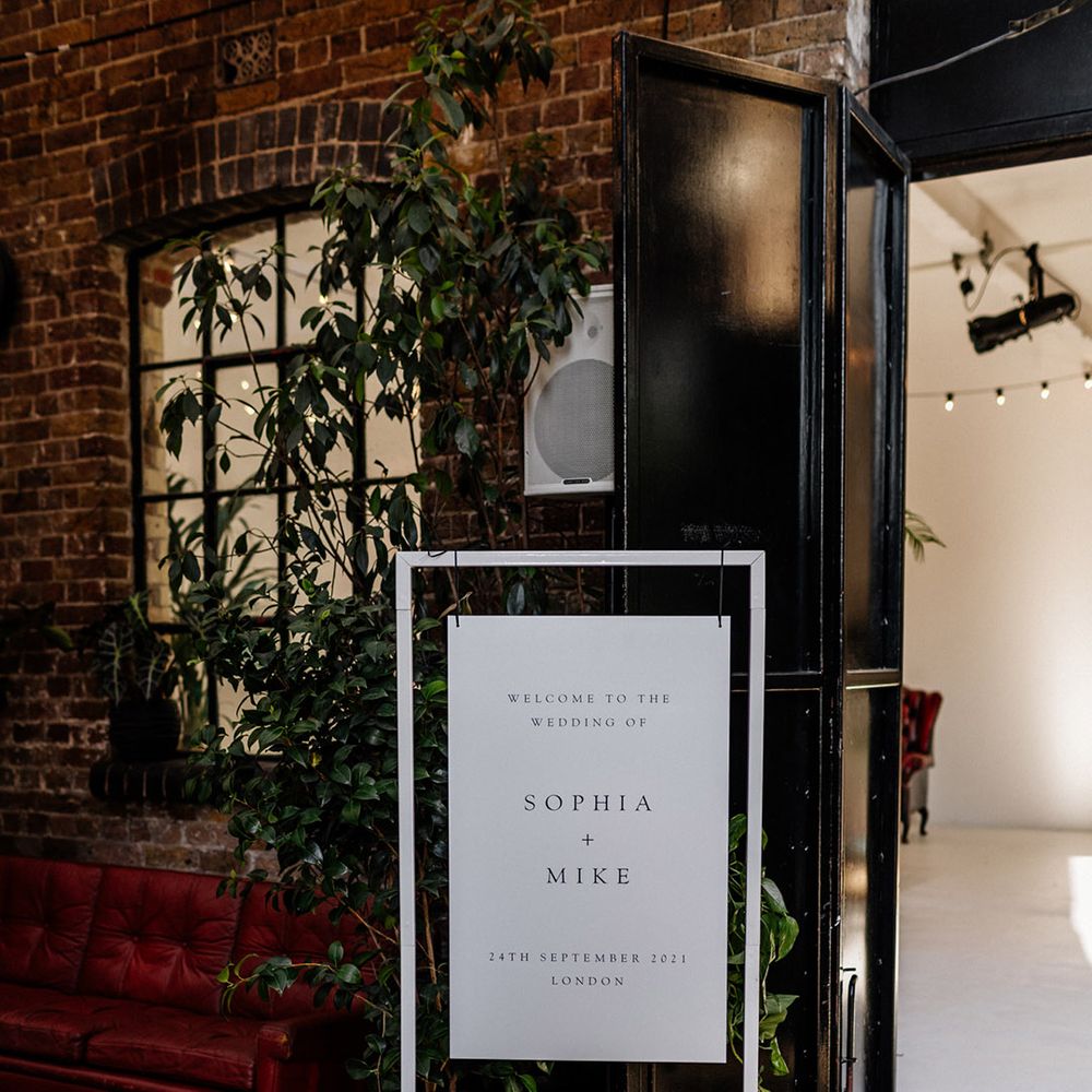 White minimalist wedding welcome sign on a white metal stand with pink pillar candles at the base 