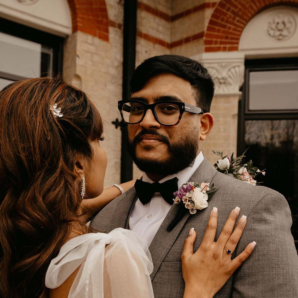Bride showing off wedding ring with groom in grey suit, black bow tie and mixed neutral boutonniere 