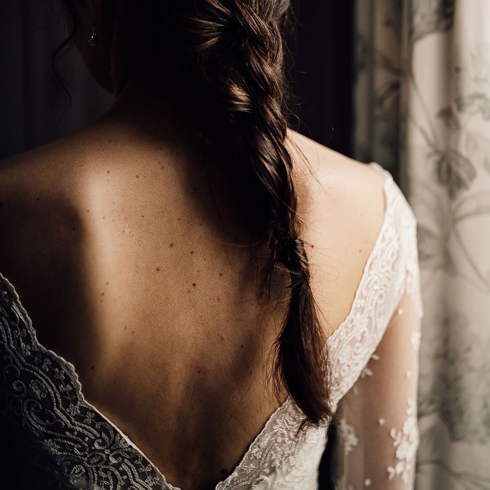 Bride with brown hair in simple braid decorated with colourful flowers wearing wedding dress with sheer lace sleeves