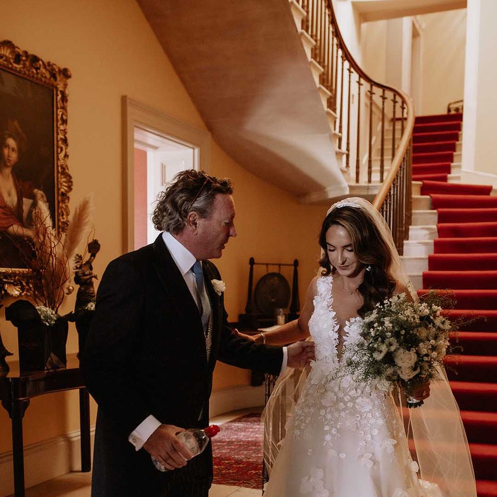 Father of the bride meets the bride at the bottom of the steps to take her to the outdoor wedding ceremony