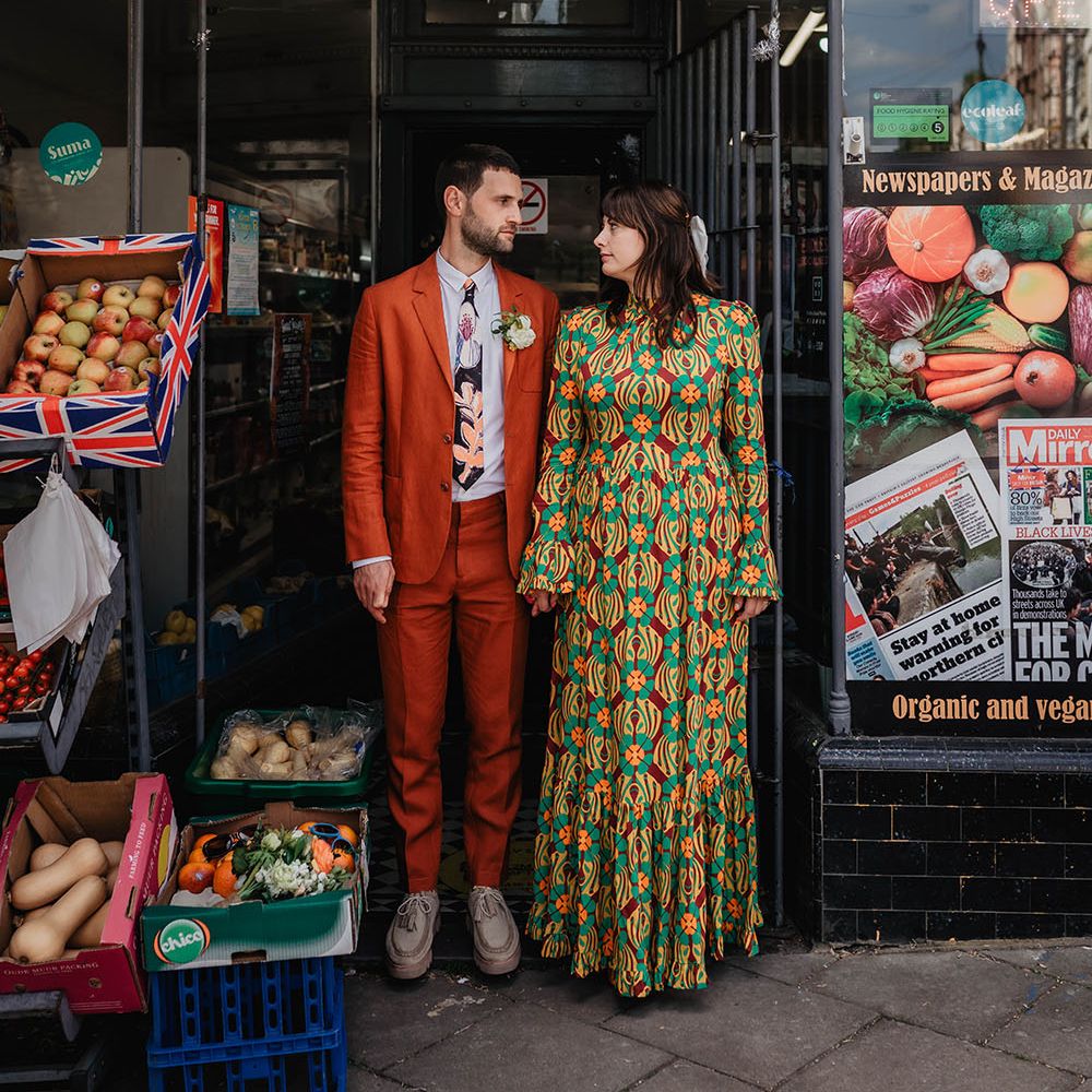 Bride & groom hold hands outdoors as groom wears orange Paul Smith linen suit complete with floral tie 