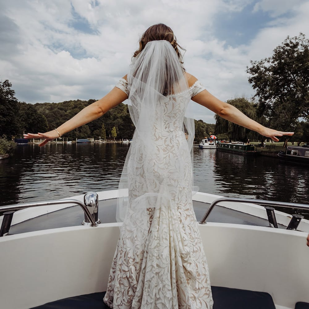 Bride in a boho lace wedding dress from Lovely Bride with a veil from Britten Weddings as she does the Titanic pose on the boat 