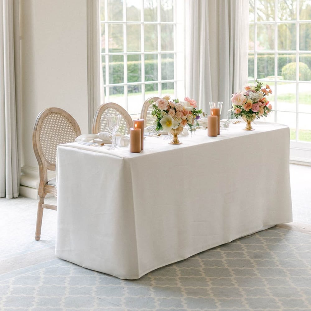 Small top table with a white tablecloth, pastel colourful wedding flower arrangements and neutral pillar candles 