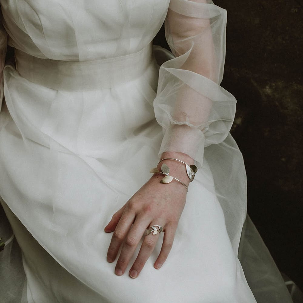Bride wearing a gold leaf bridal necklace and matching cuff bracelet with a sheer long sleeve wedding dress
