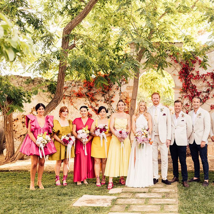 Bride and groom stands with their wedding party in bright and colourful bridesmaid dresses and cream groomsmen suits