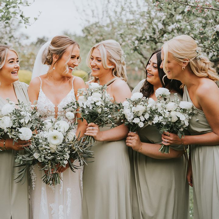 Bridesmaids in elegant sage green dresses with the bride all holding white flower wedding bouquets