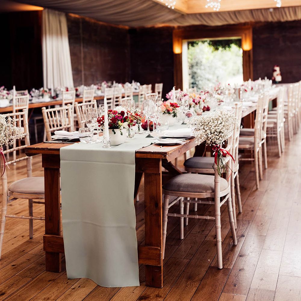 Light green table runners, tall candles, pink and red floral arrangements and hanging glass lights in reception room of Elmore Court