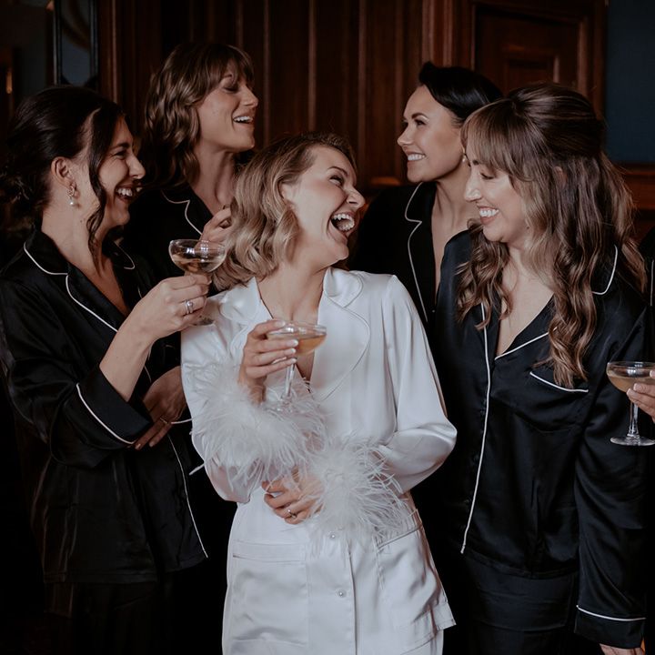 Bridesmaids in black satin pyjamas with the bride in a white satin pyjama set with feather cuffs for the morning of the wedding 